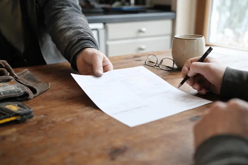 A tradesperson handing a printed estimate across a kitchen table